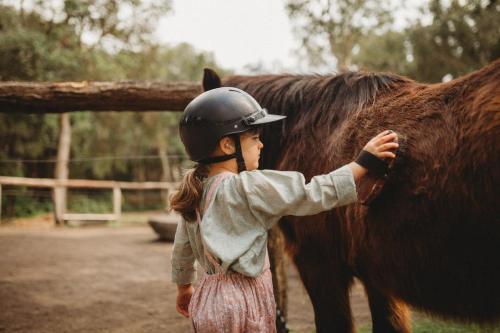 a little girl standing next to a brown horse at Elements Of Byron in Byron Bay