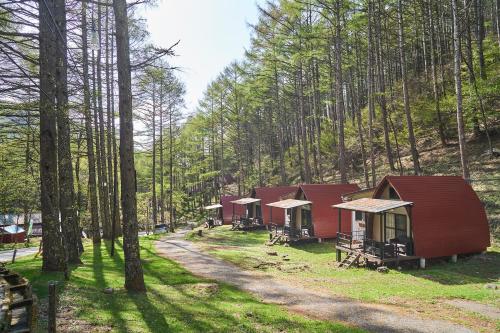a row of red cabins in a forest at Sakurashimizu Cottage/ Camp & Gramping in Matsumoto