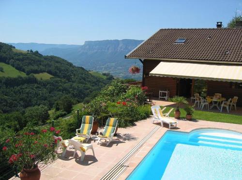 a swimming pool with chairs and a house and mountains at Chalet la Colombière in Sainte-Agnès