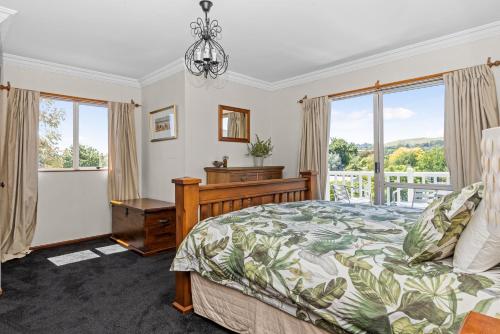 a bedroom with a bed and a desk and windows at Live Large in the Village in Havelock North