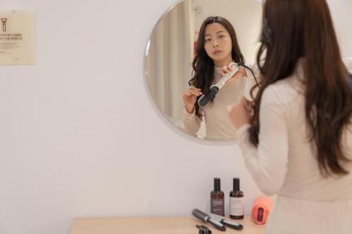 a woman brushing her hair in front of a mirror at Aank Hotel Cheonan Station 2nd in Cheonan