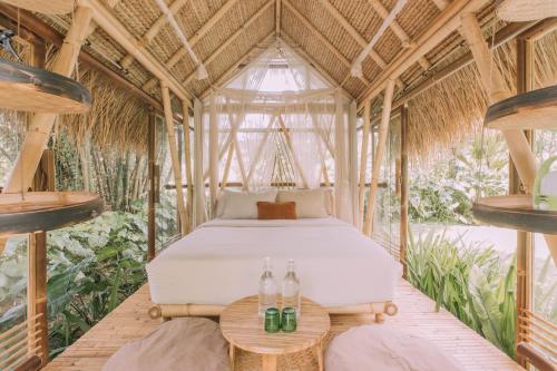 1 dormitorio en una casa de bambú con 1 cama y 2 mesas en Hideout Bali en Selat