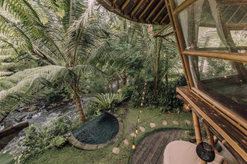 an indoor garden with a pond and palm trees at Hideout Eco Bamboo House Bali in Selat