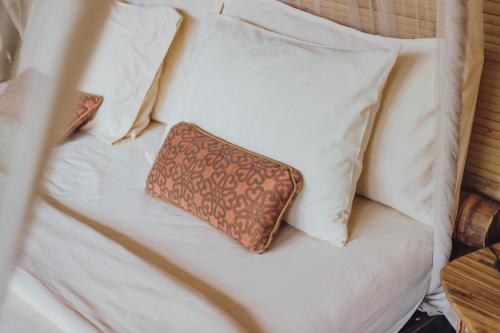 a pillow on a bed with white pillows at Hideout Eco Bamboo House Bali in Selat