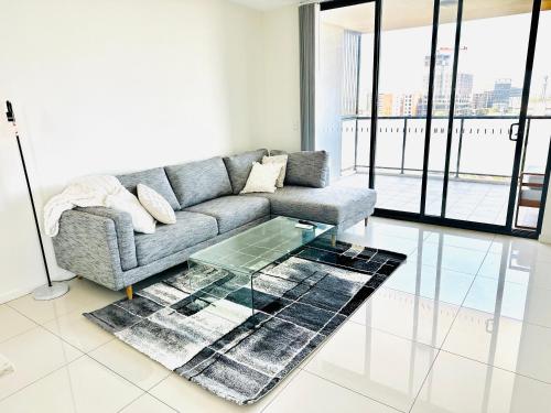 Una sala de estar con un sofá y una mesa de cristal. en Modern 2 bedroom & 2 bathroom apartment with stunning Sydney CBD & Skyline Views!, en Liverpool