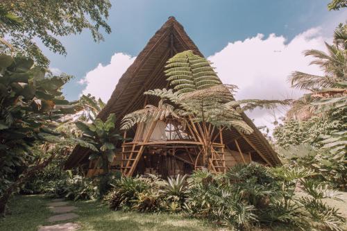 a bamboo house with a thatched roof in a garden at Hideout Eco Bamboo House Bali in Selat