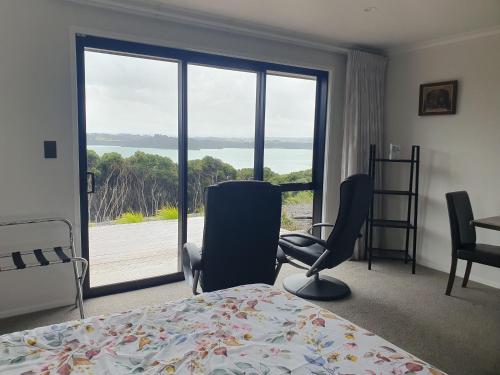 a bedroom with a bed and chairs and a large window at Makuri Bay Hideaway in Purerua