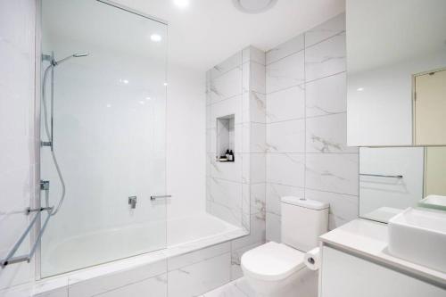 a white bathroom with a shower and a toilet at Lux 2 Bed 2 Bath Secure Parking Apartment in the Heart of Dickson, Canberra in Canberra