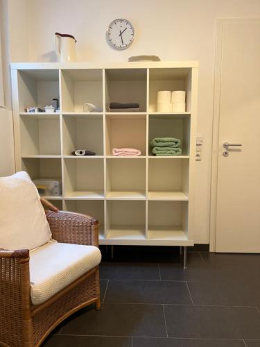 a white book shelf with a clock and a chair at privates Doppelzimmer mit separatem Eingang in Utting am Ammersee