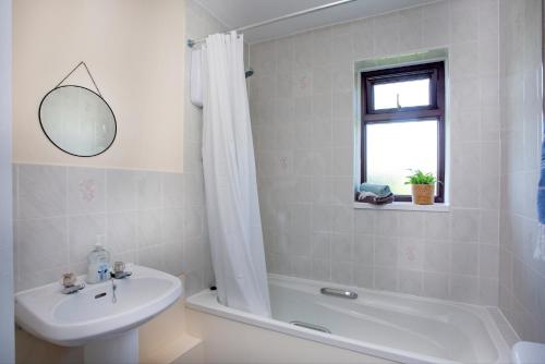 ein weißes Badezimmer mit einem Waschbecken, einer Badewanne und einem Spiegel in der Unterkunft Breezes at Stoneleigh in Seaton