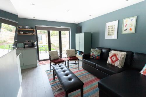 a living room with a black couch and a kitchen at Sunbeam Cottage in Whitstable