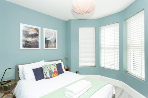 um quarto com paredes azuis, uma cama e janelas em Sunbeam and Sundance Cosy House em Whitstable