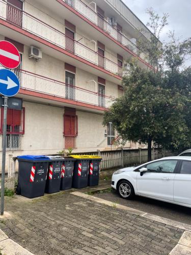 une voiture blanche garée devant un bâtiment avec des poubelles dans l'établissement De Nicolò Home, à Putignano