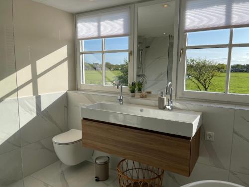 een badkamer met een wastafel, een toilet en een spiegel bij Villa Lighthouse in Callantsoog