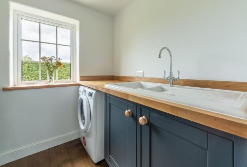 eine Küche mit blauen Schränken, einem Waschbecken und einem Fenster in der Unterkunft Heath Cottage in Mattishall