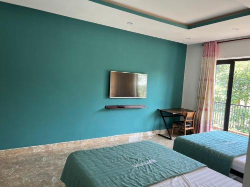 1 dormitorio con 2 camas y TV en una pared azul en PUPON Homestay and Coffee en Quang Ngai