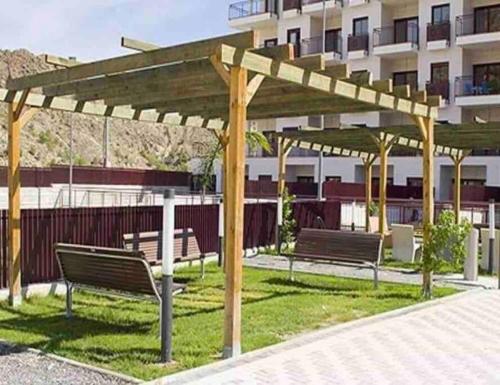 two benches under a wooden pergola in front of a building at NATUR Spa in Villanueva de Río Segura