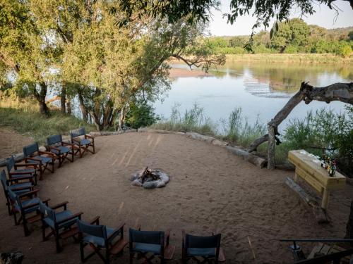 a group of chairs and a bonfire on a beach next to a lake at Hideaways Amava River Lodge, Balule, Greater Kruger in Hoedspruit