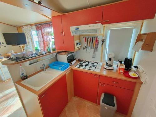uma pequena cozinha com armários vermelhos e um lavatório em Mobil home 6 personnes climatisation Sainte Croix du Verdon - Gorges du Verdon em Sainte-Croix-de-Verdon