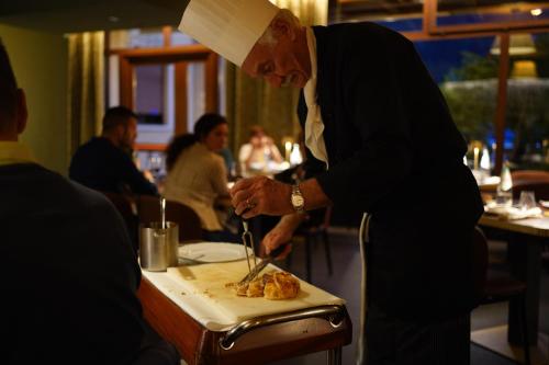 a man in a chefs hat cutting food on a table at Hotel Du Lac in Molveno