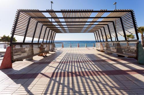 a person sitting on a boardwalk near the beach at Home2Book Comfy Apt Puertito de Güímar, Pool in Puertito de Güímar