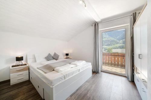 a white bedroom with a bed and a large window at Haus Tanja Apartment 3 in Parcines