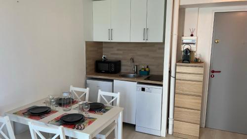 une cuisine avec une table et des chaises et une cuisine avec des armoires blanches dans l'établissement Appartement 2 pièces en rez-de-chaussée dans résidence avec accès direct à la plage, à Cabourg