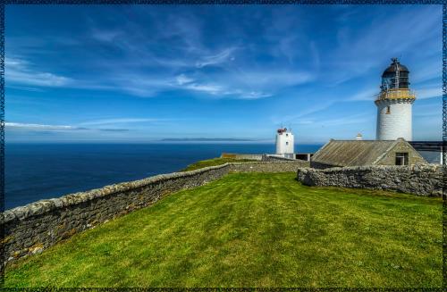 a lighthouse on top of a stone wall next to the ocean at Apartment 500 - Metro style apartment on NC500 in Thurso