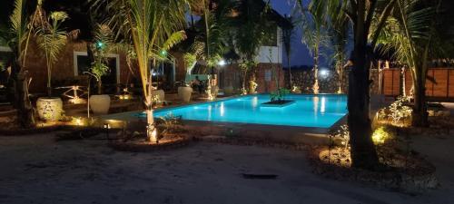 a swimming pool at night with palm trees and lights at Salama & Mbuyuni Bungalows in Matemwe