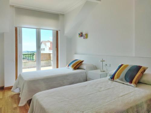 two beds in a white room with a window at Desconectaengalicia Ático La Lanzada in A Lanzada