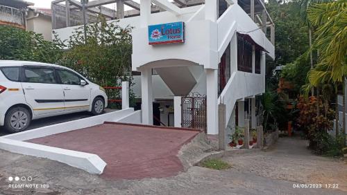 ein weißes Auto, das neben einem Gebäude mit Schild parkt in der Unterkunft The Lotus Home in Port Blair