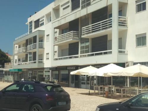 a building with tables and white umbrellas in front of it at Navigation House in Sesimbra