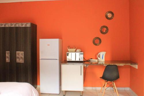 a kitchen with an orange wall with a refrigerator and a chair at 7th Dimension Guesthouse in Zeerust