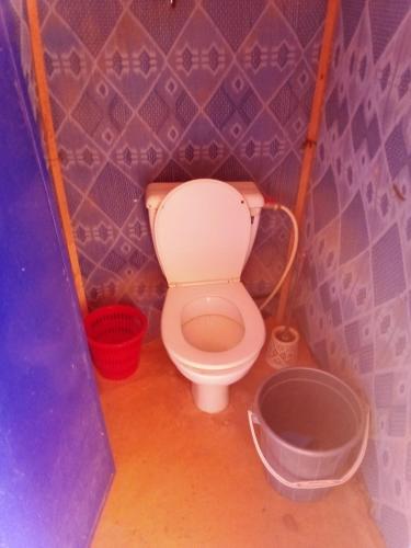 a small bathroom with a toilet and a bucket at ERG MERZOUGA SAHARA CAMP in Merzouga