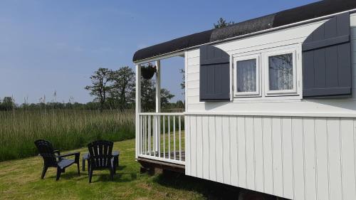 a white tiny house with two black chairs in a field at Pipowagen 't Strunerke in Augustinusga