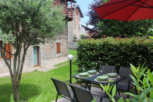 Apartment Bianca with private garden في Cossogno: طاولة سوداء وكراسي مع مظلة حمراء