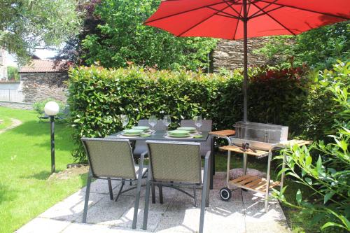 Apartment Bianca with private garden في Cossogno: طاولة وكراسي مع مظلة حمراء