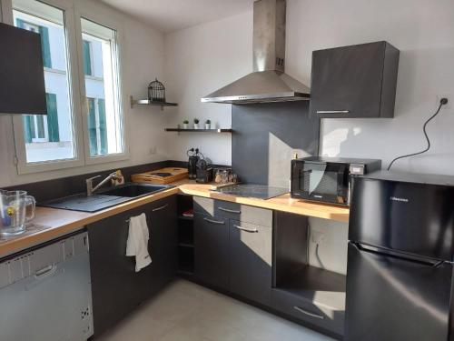 La cuisine est équipée d'un réfrigérateur noir et d'un évier. dans l'établissement La Maison bleue des Mathes, aux Mathes