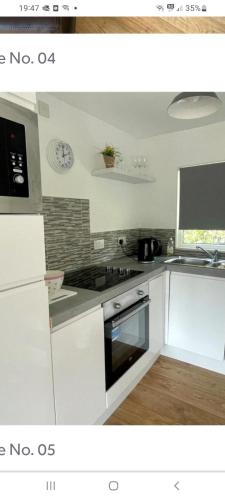 a kitchen with white cabinets and a stove top oven at Sunny49 min 3 night stay in Caeathro
