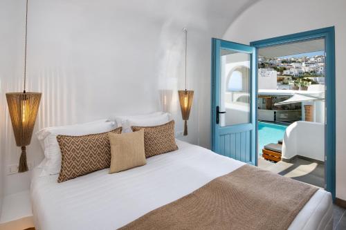 a bedroom with a white bed with pillows and a blue door at Evgenia Villas & Suites by Calm Collection in Fira