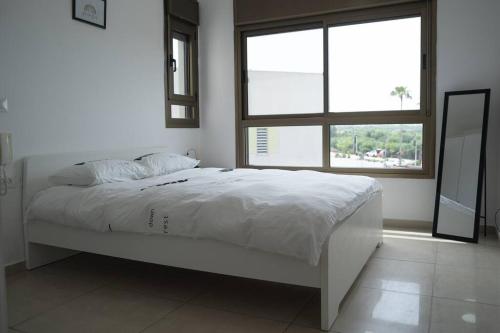 ein weißes Bett in einem Zimmer mit einem großen Fenster in der Unterkunft Unique beach apartment in Rischon LeZion