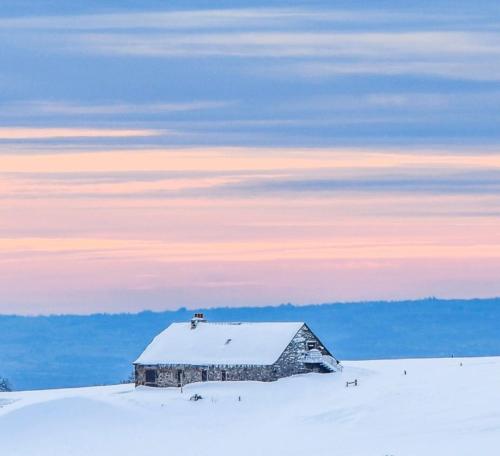 un antiguo granero en un campo cubierto de nieve con un cielo en Studio au cœur de Laguiole en Laguiole