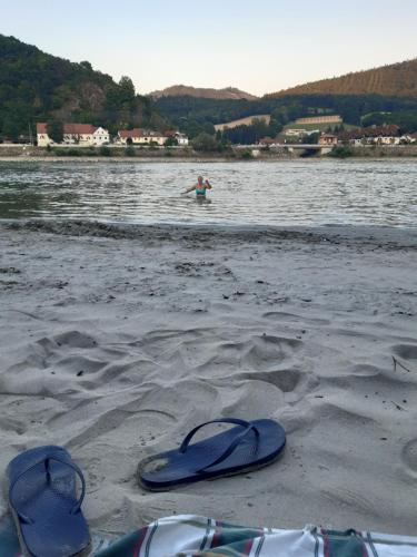 a pair of flip flops on a beach with a person in the water at Goldene Wachau - Privatzimmer in Aggsbach
