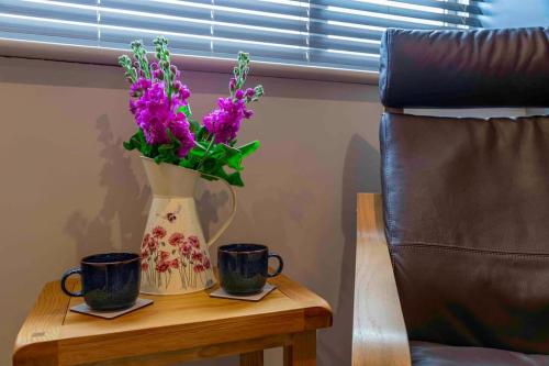 a table with two cups and a vase with purple flowers at Wensleydale Halls in Leyburn