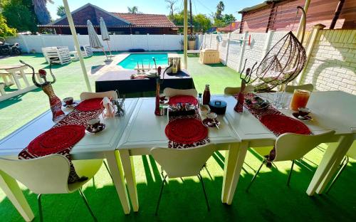 uma mesa branca com pratos e cadeiras vermelhas e uma piscina em Swane’s guesthouse em Rustenburg