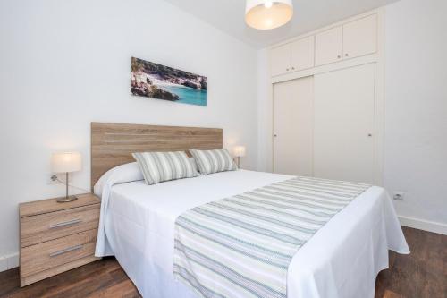 - une chambre avec un lit blanc et une tête de lit en bois dans l'établissement Apartamentos Llebeig, à Ciutadella