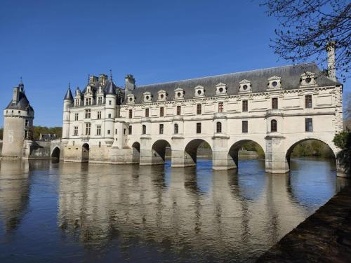 un castillo grande con un puente sobre un río en Chambre d'hôtes proche Chenonceau en Chisseaux
