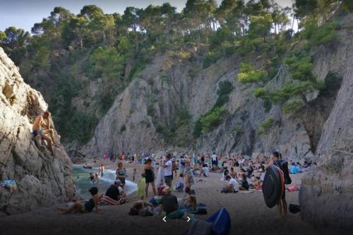 a crowd of people sitting on a beach near a cliff at Appartement tout confort avec WIFI vue sur mer et piscine communautaire secteur EL GOLFET à Callela de Palafrugell in Palafrugell