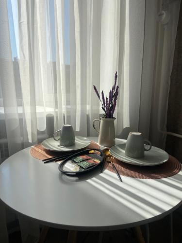 una mesa blanca con dos platos y un jarrón con flores en Комфортабельные - Уютные апартаменты в Костанай Алтын Арман en Kostanái