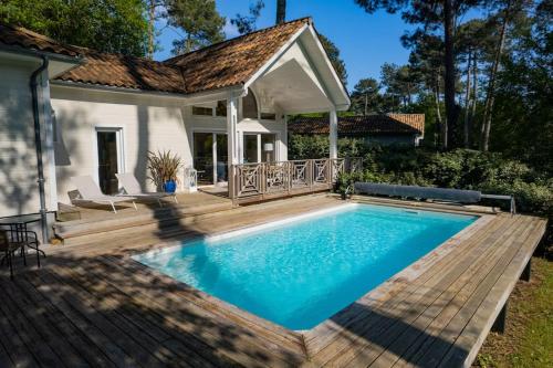 une piscine avec une terrasse en bois et une maison dans l'établissement Villa calme du golf avec piscine proche du lac, à Biscarrosse